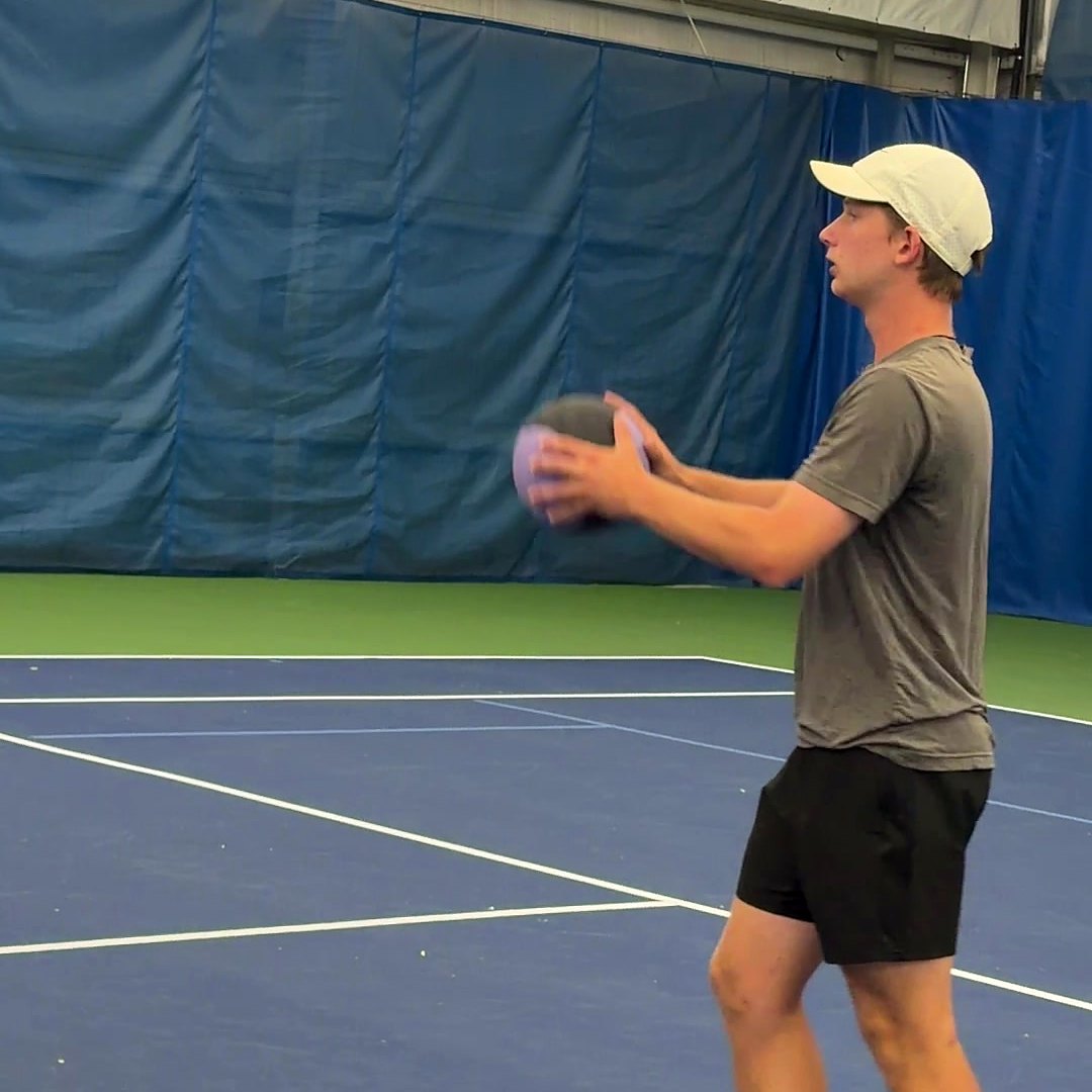 A coach leading a medicine ball drill in front of the Quad City Tennis Club banner