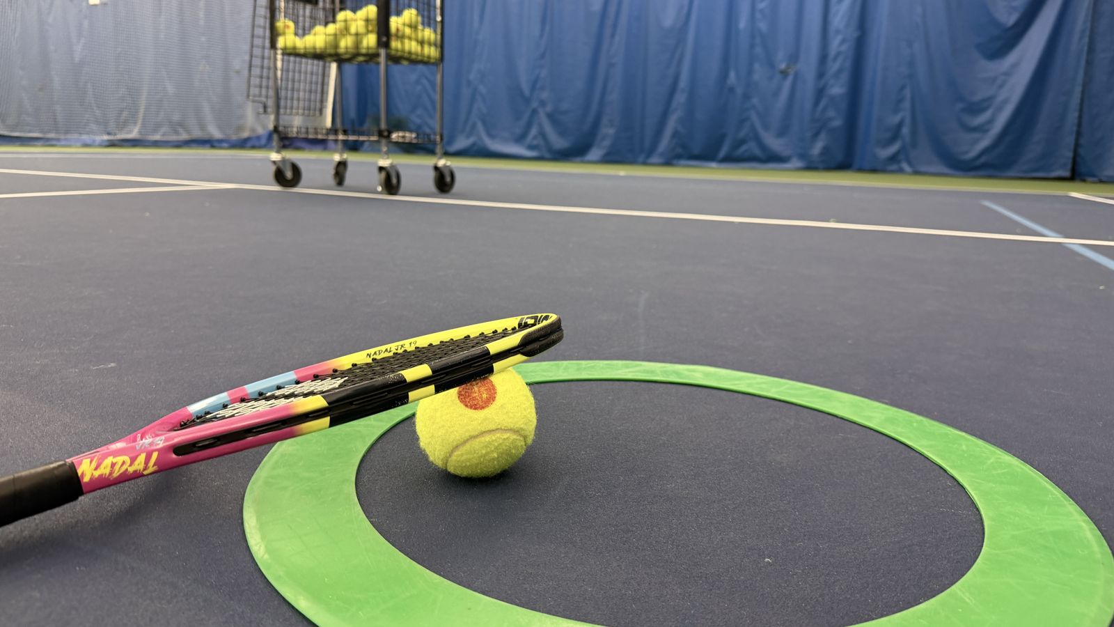 A junior racquet and tennis ball resting on a green target ring on the court