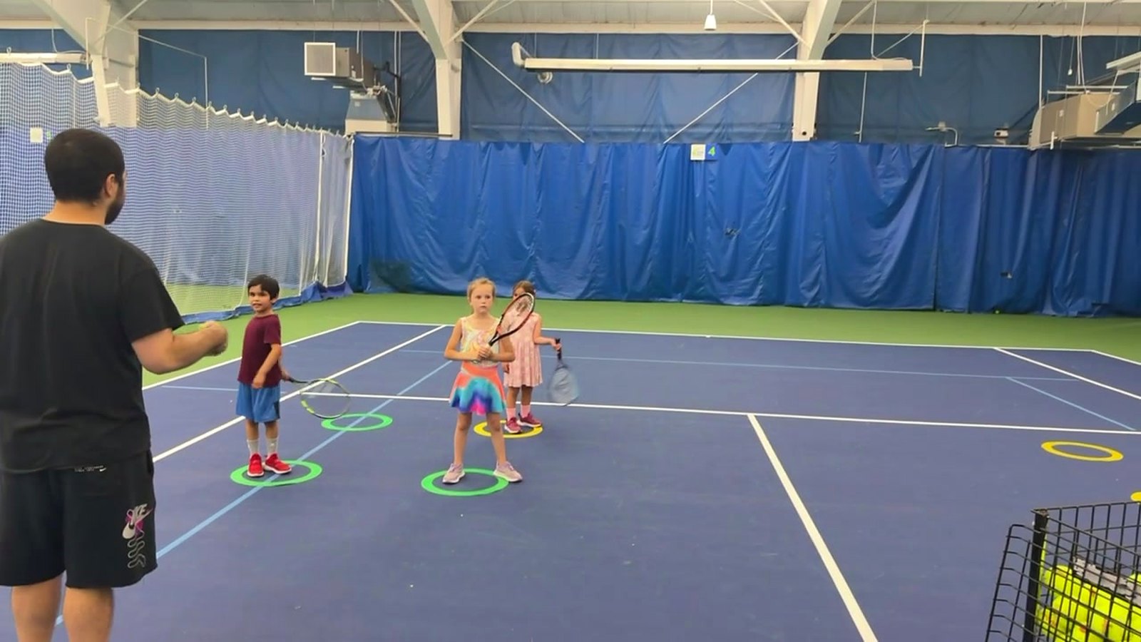 A coach leading young kids in a beginner tennis class on the indoor courts at the Quad City Tennis Club