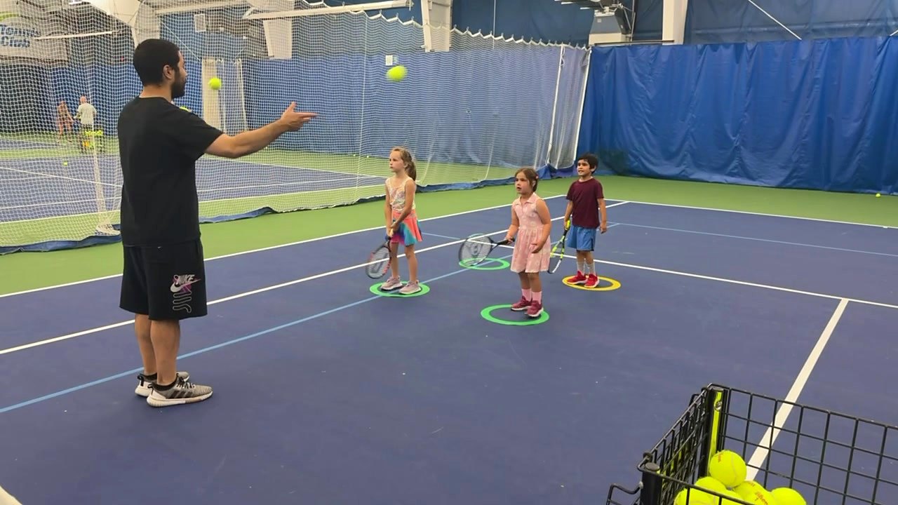 A coach working with a line of young players during a youth tennis class