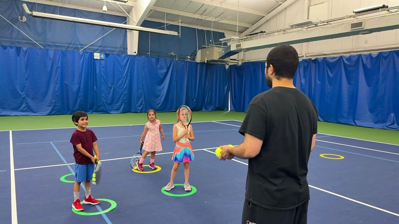 Young players holding racquets in their hoops while a coach demonstrates during a youth class