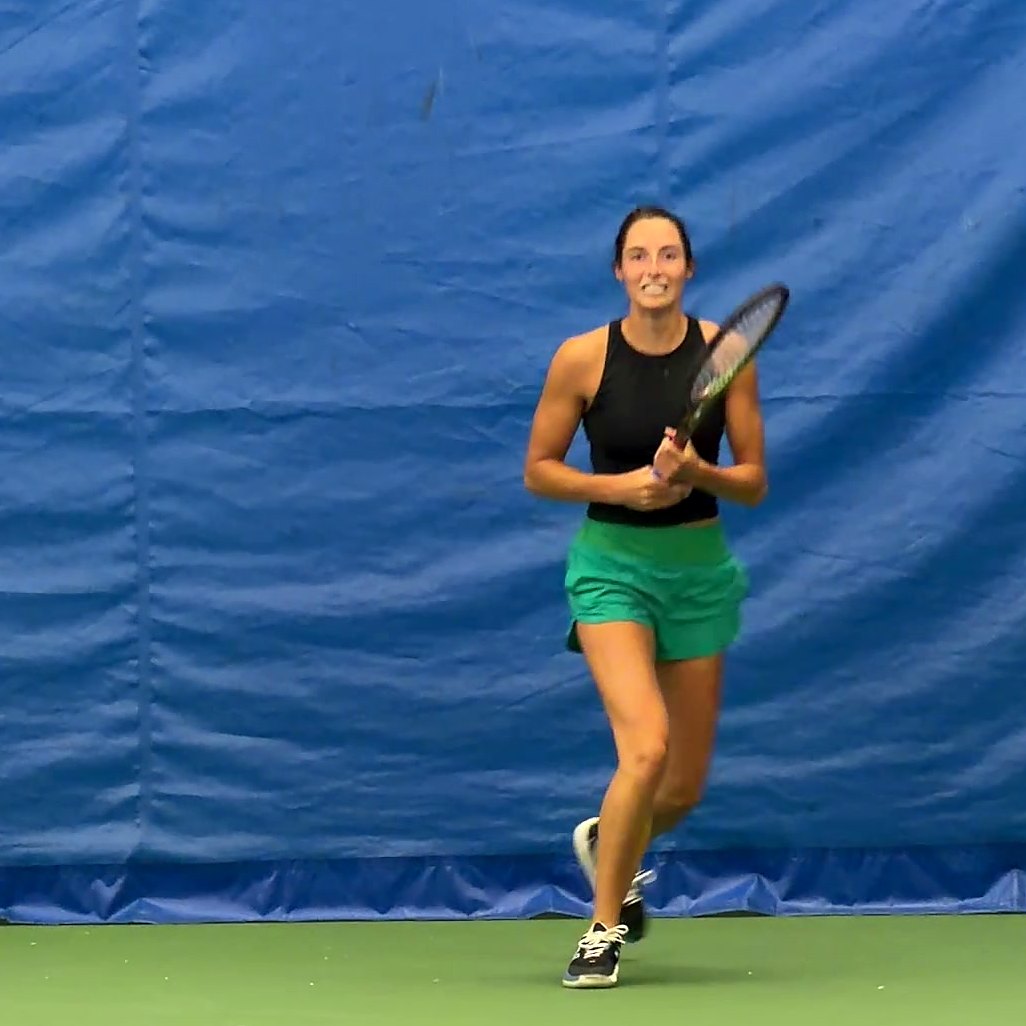 A smiling player ready at the baseline on an indoor court
